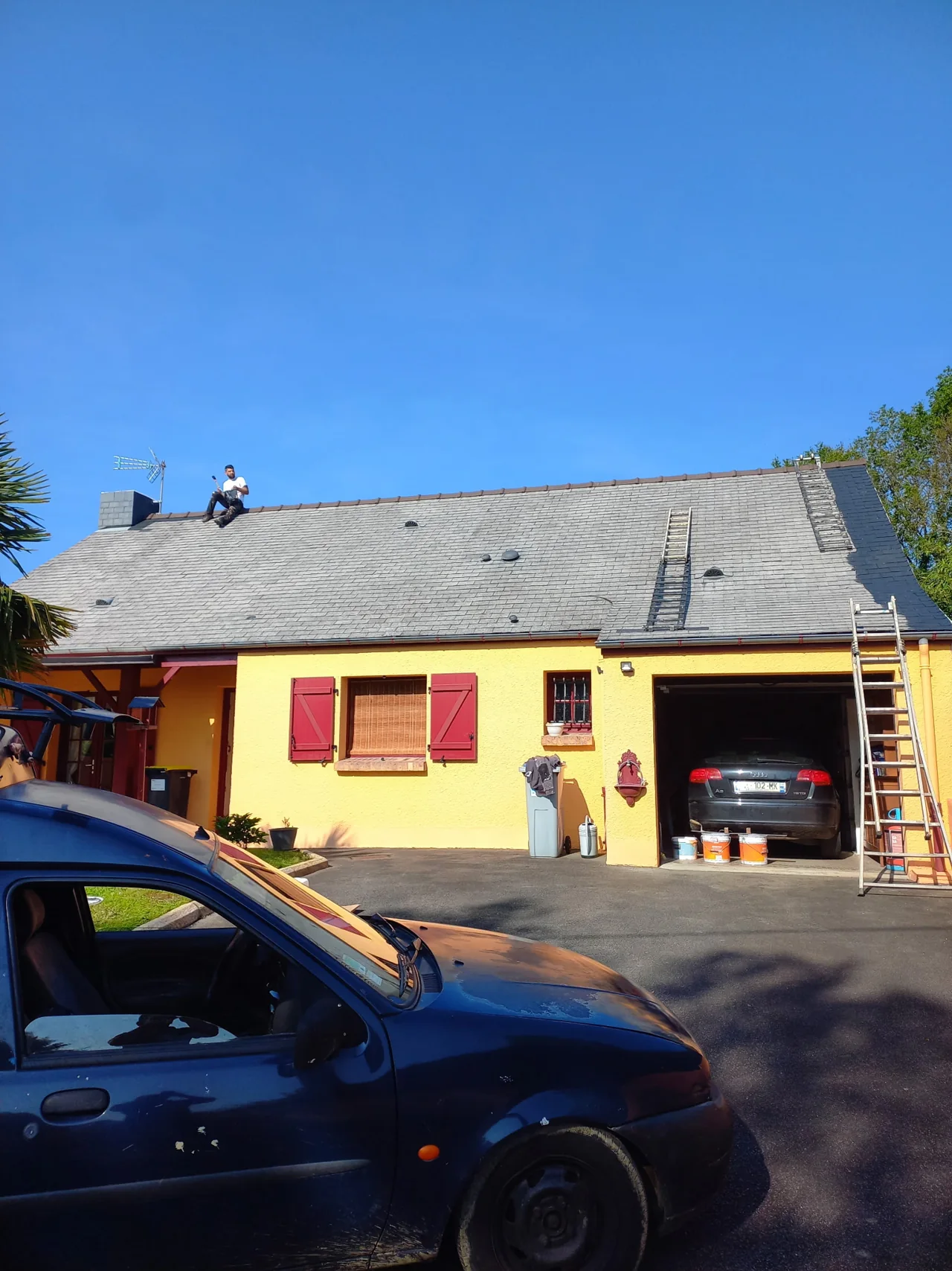 Artisan sur la toiture d’une maison jaune avec des volets rouges