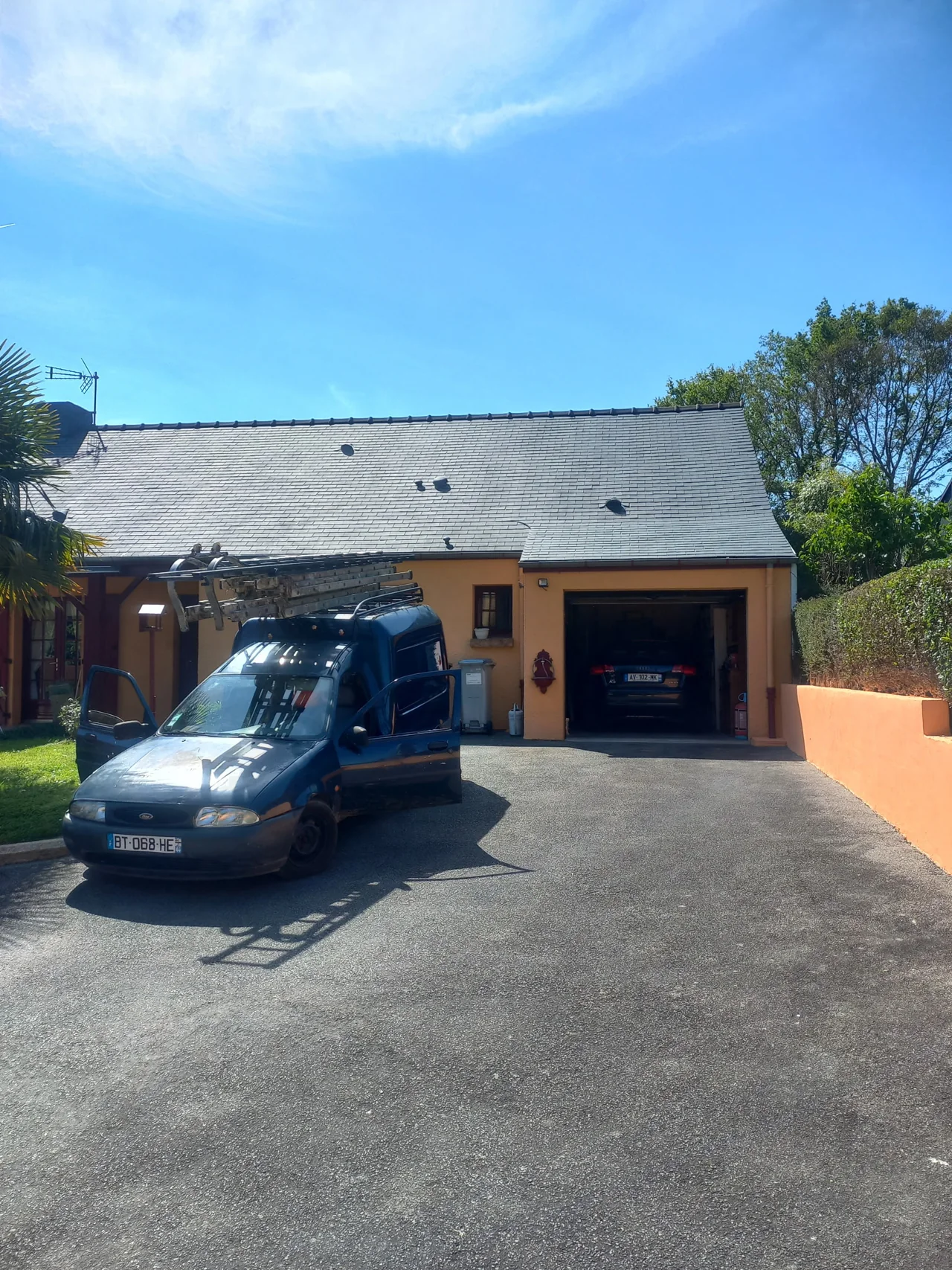 Toiture d’une maison jaune avec une camionnette et des échelles devant la façade